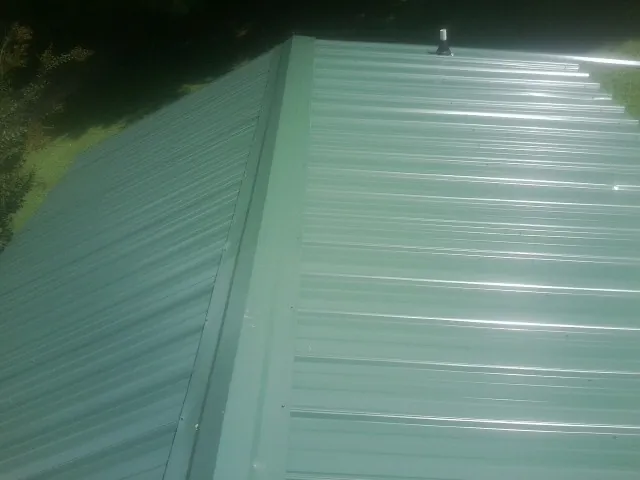 New green metal panels meeting at the ridge of a roof — Flat Roof Repair work by our crew in Urbana
